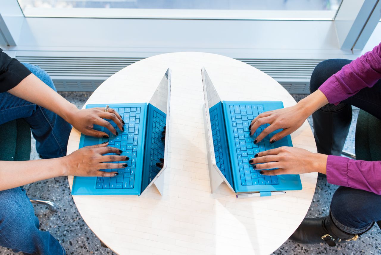 Two people working on blue laptops at a round table, focusing on teamwork and technology.