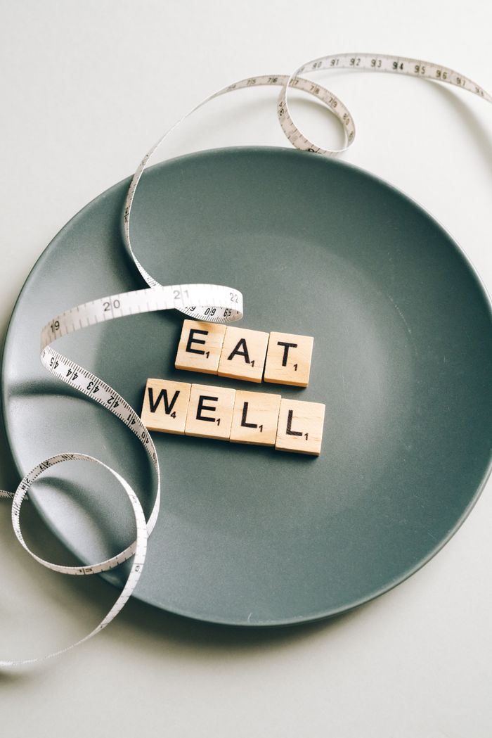 Creative photo of 'Eat Well' letter tiles on a plate with measuring tape, symbolizing balanced nutrition.