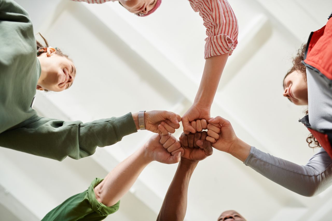 Four diverse team members join fists together, displaying unity and teamwork.